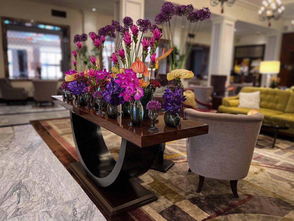 A decorative table featuring an array of vibrant flowers in various colors, including purple, pink, and orange, displayed in elegant vases, set in a stylish lobby space.
