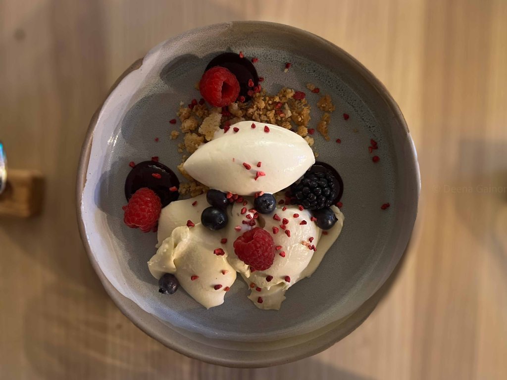 A dessert bowl featuring creamy ice cream topped with fresh raspberries, blueberries, and blackberries, alongside crunchy granola and decorative raspberry crumbs.