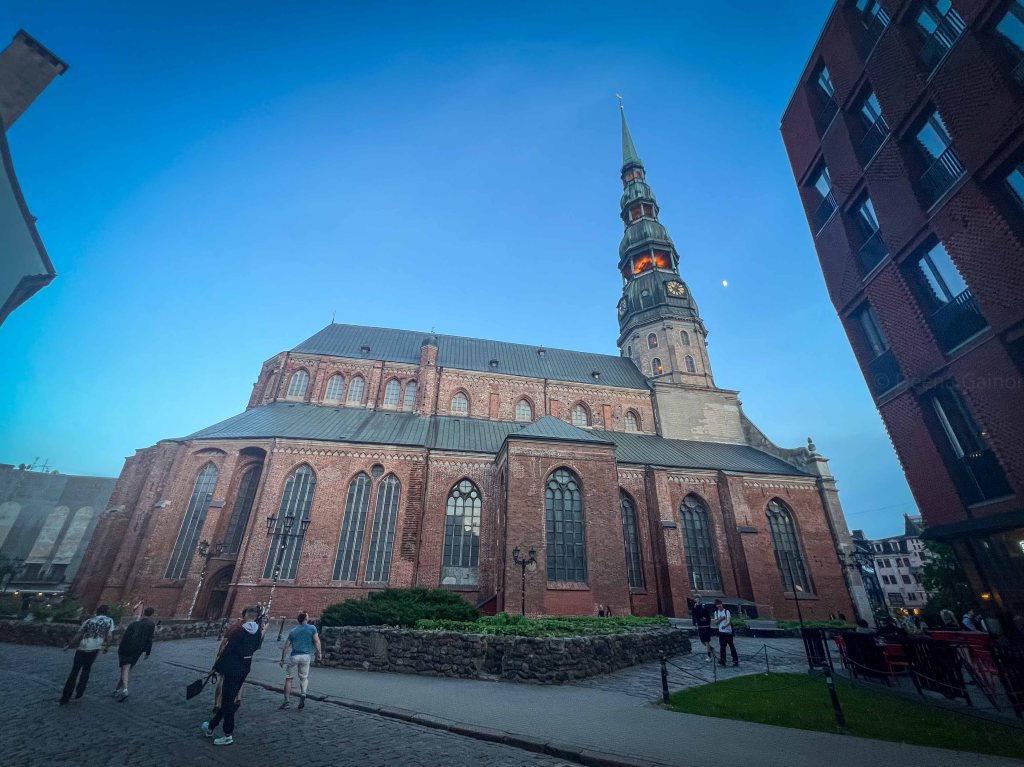 A historic brick church with a tall, pointed steeple, surrounded by people walking in an urban setting during twilight.