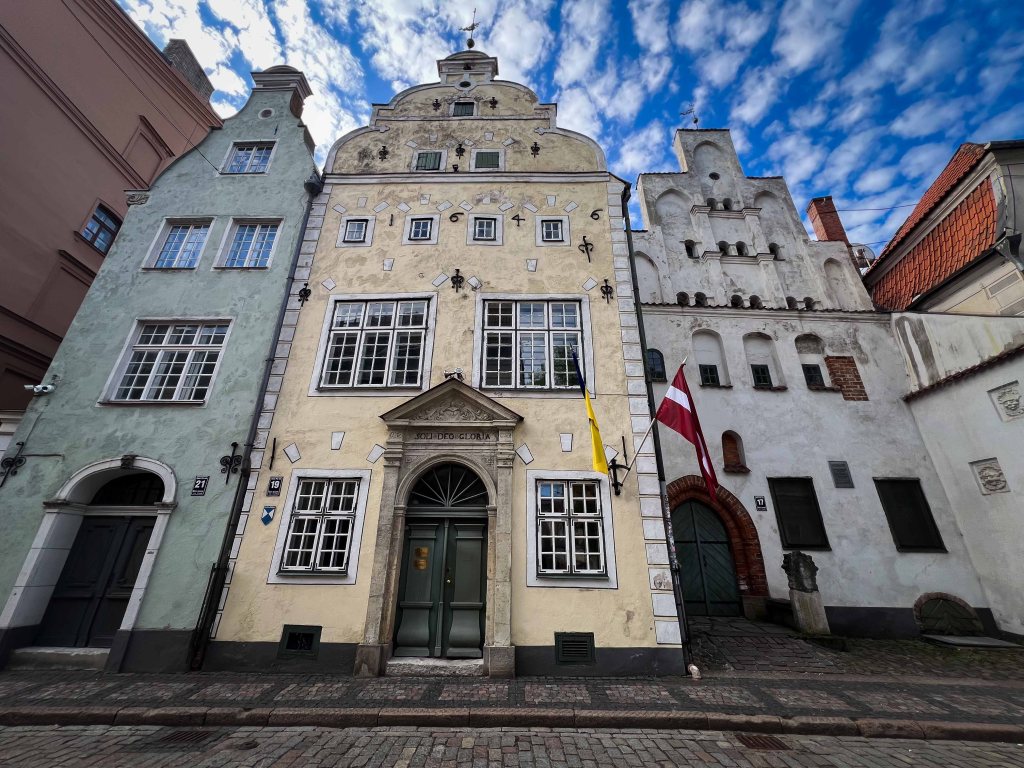 A charming collection of historic buildings in a row, featuring different colors and architectural styles, with a blue sky and scattered clouds in the background.