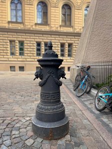 A decorative black fire hydrant in a cobblestone area with bicycles parked nearby.