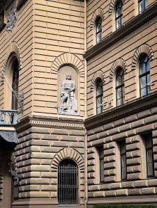 Close-up of a historic building corner featuring ornate architectural details and a prominent sculpture set in the wall.