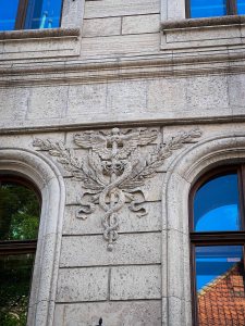 A decorative stone relief on a building facade featuring an eagle with wings spread, intertwined with a caduceus symbol.