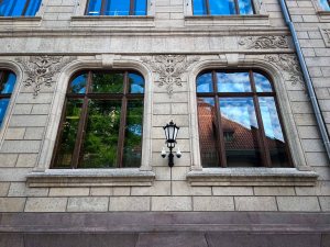 Close-up of a historic building's facade featuring ornate window frames, decorative carvings, and a vintage wall lamp.