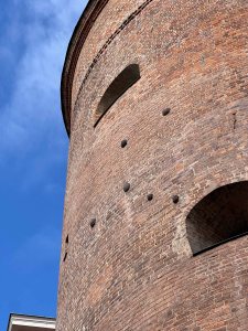 Close-up view of a brick tower featuring several circular openings and weathered brickwork against a clear blue sky.