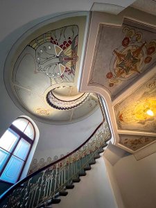 Elegant spiral staircase with ornate ceiling and decorative wall art.