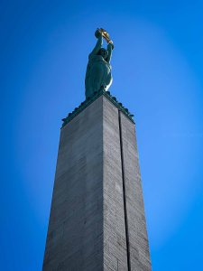 A tall monument featuring a statue holding a golden object, set against a clear blue sky.