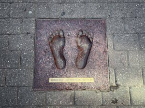 Bronze plaque featuring the cast of two bare feet embedded in a stone walkway.